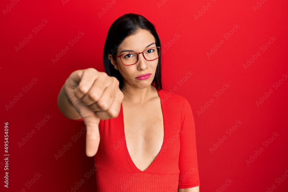 Young latin woman wearing casual clothes and glasses looking unhappy and angry showing rejection and negative with thumbs down gesture. bad expression. Young latin woman wearing casual clothes and glasses looking unhappy and angry showing rejection and negative with thumbs down gesture. bad expression.