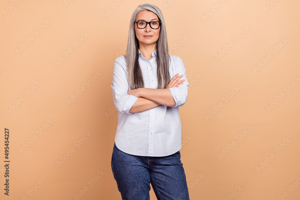 Photo of mature woman wear eyeglasses crossed hands banker smart casual isolated over beige color background Photo of mature woman wear eyeglasses crossed hands banker smart casual isolated over beige color background
