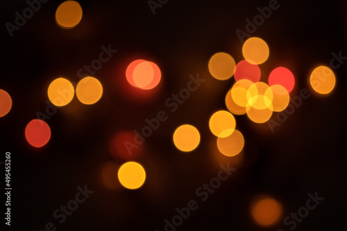 Defocused bokeh lights on black background, an abstract naturally blurred backdrop for Christmas eve or birthday party. Festive light texture. Yellow and red garland in blur. Overlay effect for design