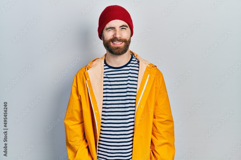 Caucasian man with beard wearing yellow raincoat winking looking at the camera with sexy expression, cheerful and happy face. Caucasian man with beard wearing yellow raincoat winking looking at the camera with sexy expression, cheerful and happy face.