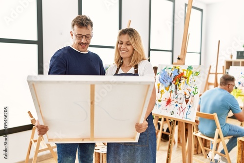 Group of middle age people drawing at art studio. Two students smiling happy holding canvas.