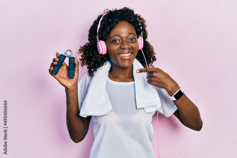 Young african american woman wearing workout clothes and holding hand grip smiling happy pointing with hand and finger Young african american woman wearing workout clothes and holding hand grip smiling happy pointing with hand and finger