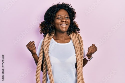 Young african american woman training with battle rope screaming proud, celebrating victory and success very excited with raised arm © Krakenimages.com