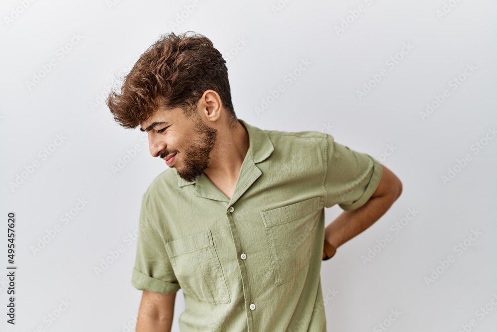 Young arab doctor man standing over isolated background suffering of backache, touching back with hand, muscular pain Young arab doctor man standing over isolated background suffering of backache, touching back with hand, muscular pain