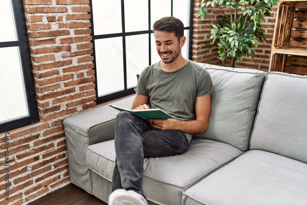 Young hispanic man smiling confident reading book at home
