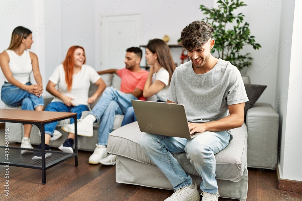 Group of young friends speaking sitting on the sofa. Man smilimg happy and using laptop at home. Group of young friends speaking sitting on the sofa. Man smilimg happy and using laptop at home.
