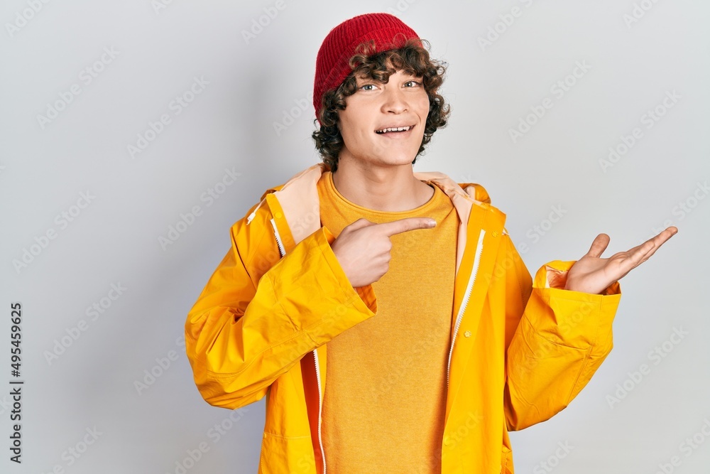 Handsome young man wearing yellow raincoat amazed and smiling to the camera while presenting with hand and pointing with finger. Handsome young man wearing yellow raincoat amazed and smiling to the camera while presenting with hand and pointing with finger.