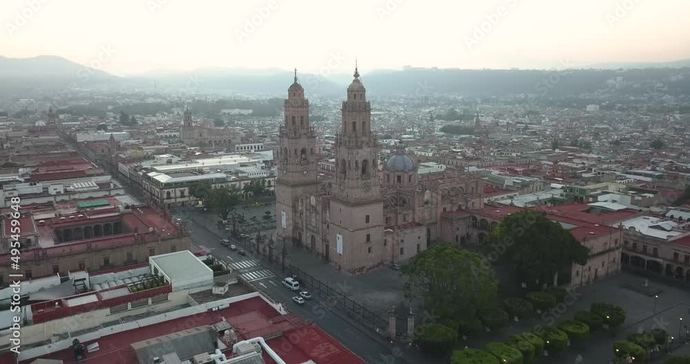 Drone flies over Morelia, Michoacan, Mexico at sunrise. Static drone shot of the main cathedral and plaza as the sun rises with the mountains in the background. Drone flies over Morelia, Michoacan, Mexico at sunrise. Static drone shot of the main cathedral and plaza as the sun rises with the mountains in the background.