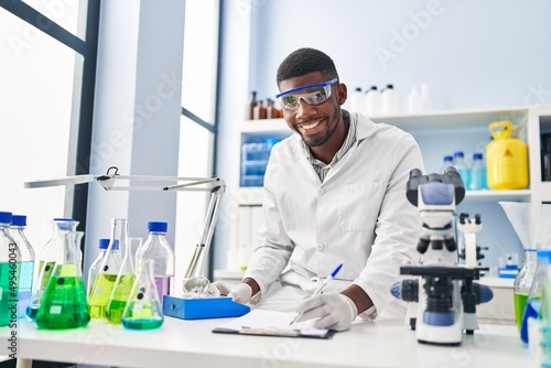 Young african american man wearing scientist uniform weighing diamond at laboratory