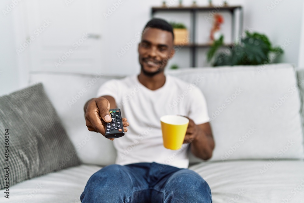 Young african american man watching tv drinking coffee at home