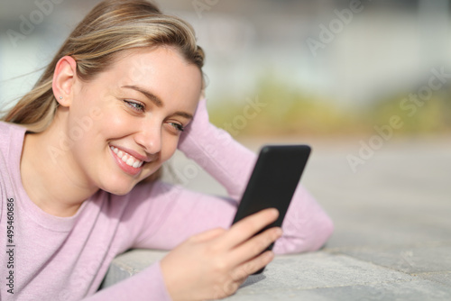 Happy teen smiling using phone in the street