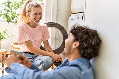 Young couple smiling happy drinking coffee while doing laundry at home.