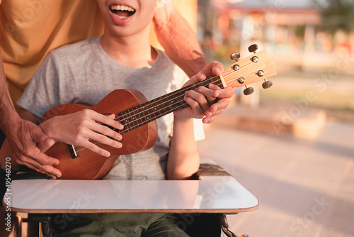 Hand of young man with disability holding ukulele and singing, playing with music therapy on the outdoor nature background,Vacation hobby activity with family activity and mental health concept.