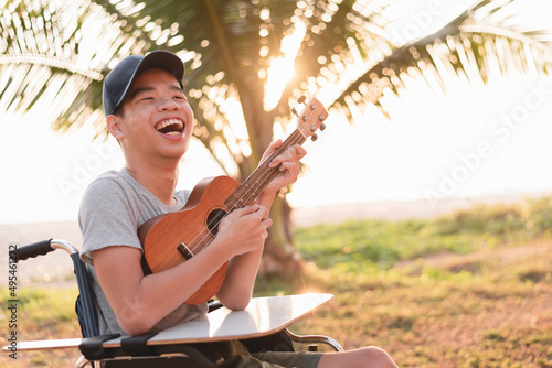 Happy face of young man with disability holding ukulele and singing, playing with music therapy on the outdoor nature background,Vacation hobby activity with family activity and mental health concept.