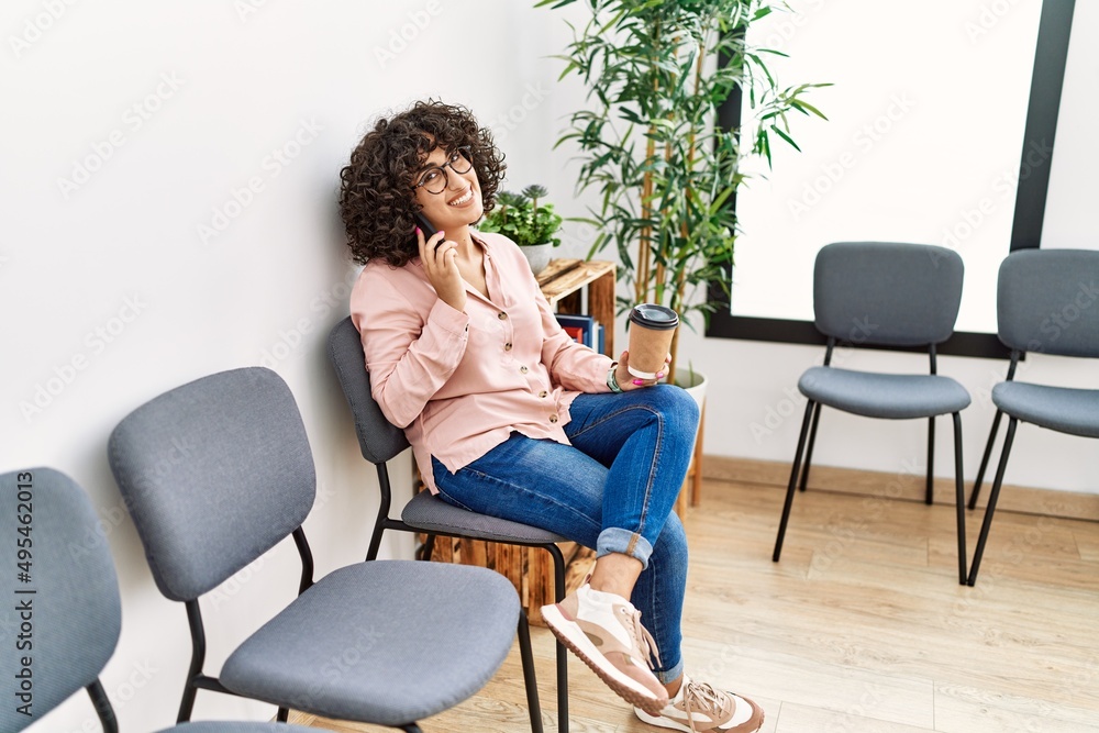 Fototapeta premium Young middle east woman talking on the smartphone drinking coffee at waiting room