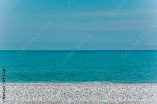 Pebble coastline and bright blue sea water and sky background. 