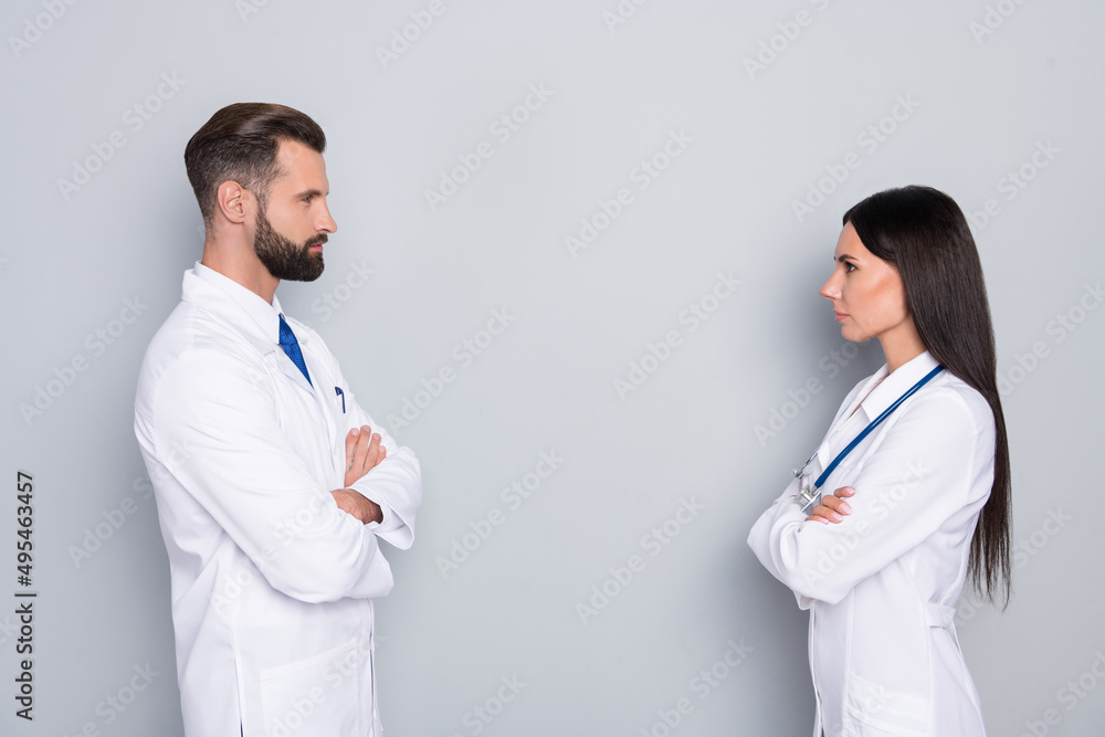 Profile side view portrait of two attractive smart doctors folded arms vs therapy isolated over grey color pastel background Profile side view portrait of two attractive smart doctors folded arms vs therapy isolated over grey color pastel background