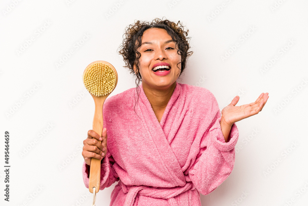 Young hispanic woman holding a back scratcher isolated on white background receiving a pleasant surprise, excited and raising hands. Young hispanic woman holding a back scratcher isolated on white background receiving a pleasant surprise, excited and raising hands.