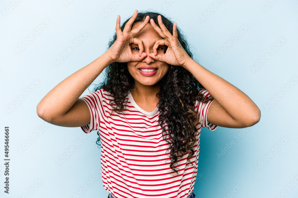Young hispanic woman isolated on blue background excited keeping ok gesture on eye. Young hispanic woman isolated on blue background excited keeping ok gesture on eye.