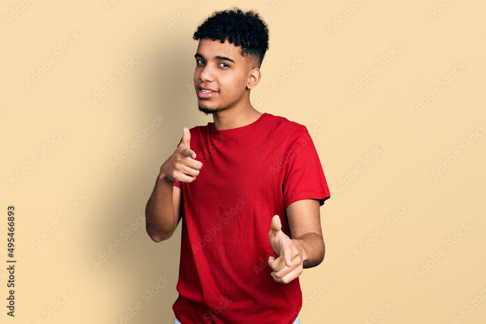 Young african american man wearing casual red t shirt pointing fingers to camera with happy and funny face. good energy and vibes. Young african american man wearing casual red t shirt pointing fingers to camera with happy and funny face. good energy and vibes.
