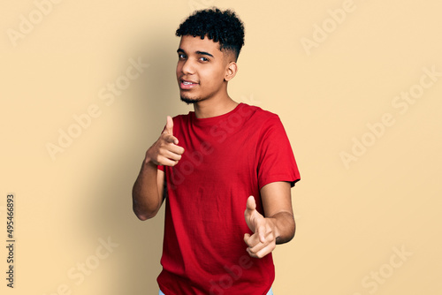 Young african american man wearing casual red t shirt pointing fingers to camera with happy and funny face. good energy and vibes.