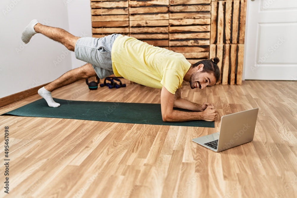 Handsome hispanic man training looking at video tutorial on laptop at the gym Handsome hispanic man training looking at video tutorial on laptop at the gym