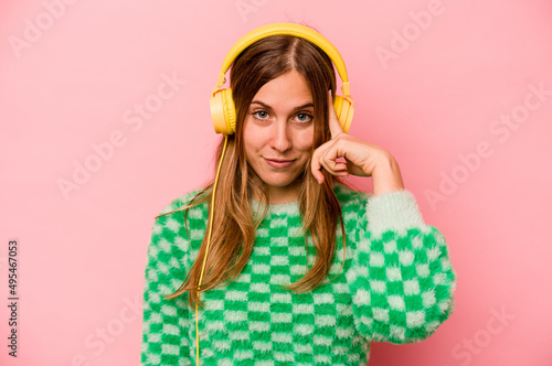 Young caucasian woman listening to music isolated on pink background pointing temple with finger, thinking, focused on a task.