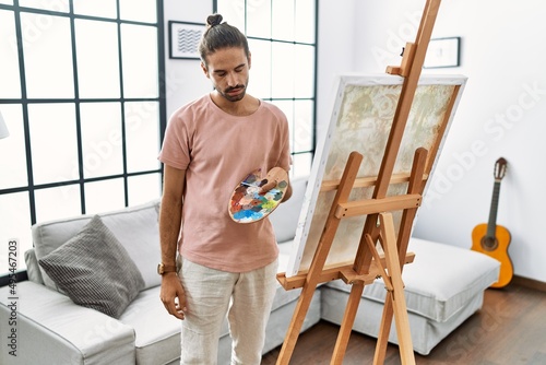 Young hispanic man with beard painting on canvas at home looking sleepy and tired, exhausted for fatigue and hangover, lazy eyes in the morning.