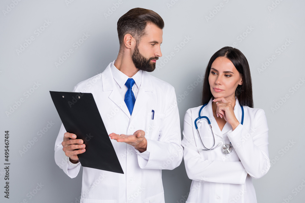 Portrait of two attractive skilled smart doctors reading analyzing illness history career isolated over grey color pastel background Portrait of two attractive skilled smart doctors reading analyzing illness history career isolated over grey color pastel background