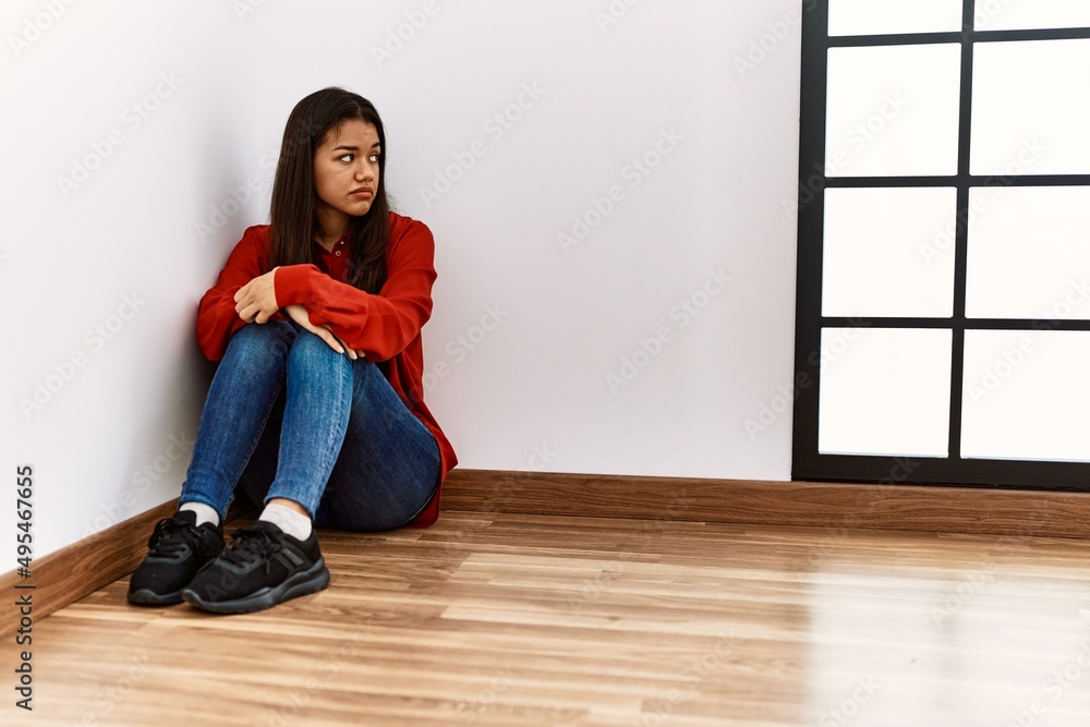 Young latin woman with serious expression sitting on the floor at empty room