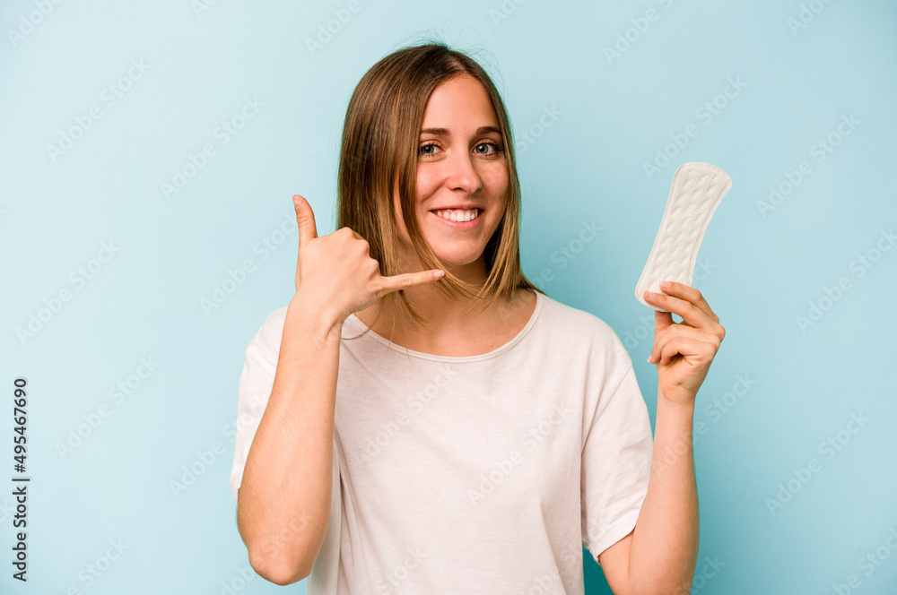 Young caucasian woman holding sanitary napkin isolated on blue background showing a mobile phone call gesture with fingers. Young caucasian woman holding sanitary napkin isolated on blue background showing a mobile phone call gesture with fingers.