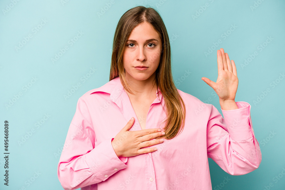Young caucasian woman isolated on blue background taking an oath, putting hand on chest.