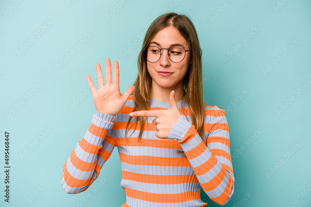 Young caucasian woman isolated on blue background smiling cheerful showing number five with fingers. Young caucasian woman isolated on blue background smiling cheerful showing number five with fingers.