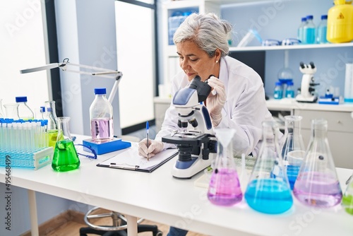 Middle age woman wearing scientist uniform write on document at laboratory