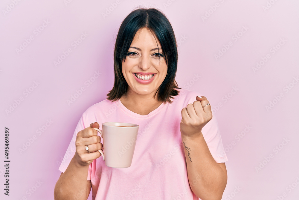 Young hispanic woman drinking a cup of coffee screaming proud, celebrating victory and success very excited with raised arm Young hispanic woman drinking a cup of coffee screaming proud, celebrating victory and success very excited with raised arm