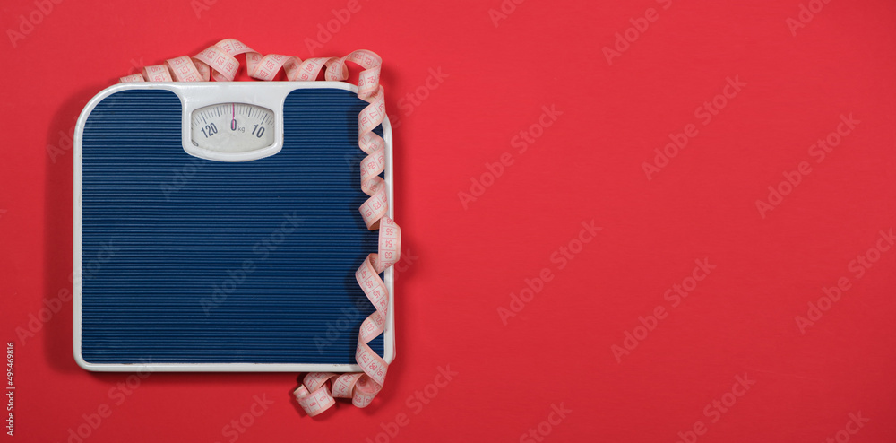 Floor blue scales and centimeter measuring tape on a red background, top view. The concept of weight loss and weight control Floor blue scales and centimeter measuring tape on a red background, top view. The concept of weight loss and weight control