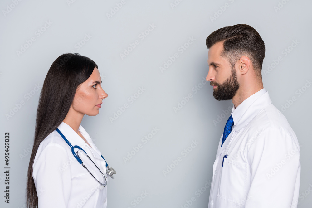 Photo of attractive smart two docs dressed white uniform looking each other isolated grey color background Photo of attractive smart two docs dressed white uniform looking each other isolated grey color background
