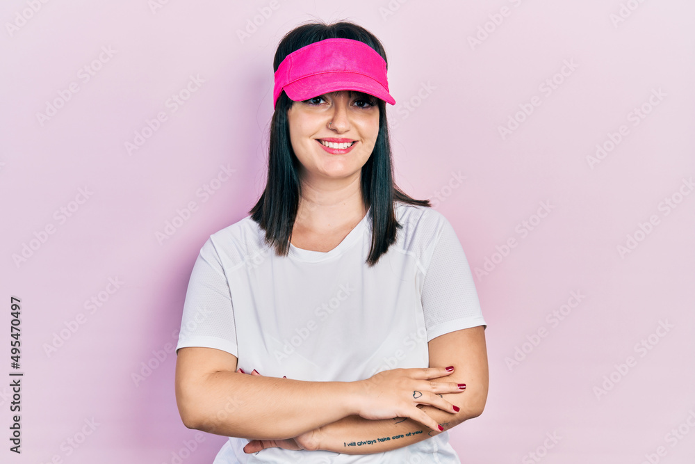 Young hispanic woman wearing sportswear and sun visor cap happy face smiling with crossed arms looking at the camera. positive person.