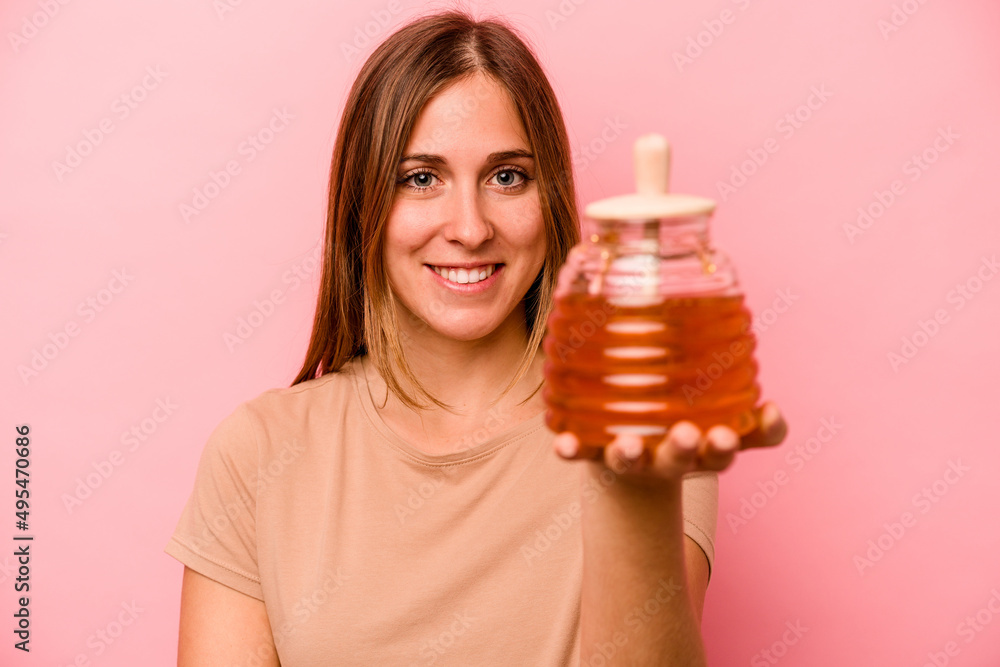 Young caucasian woman holding honey isolated on pink background Young caucasian woman holding honey isolated on pink background