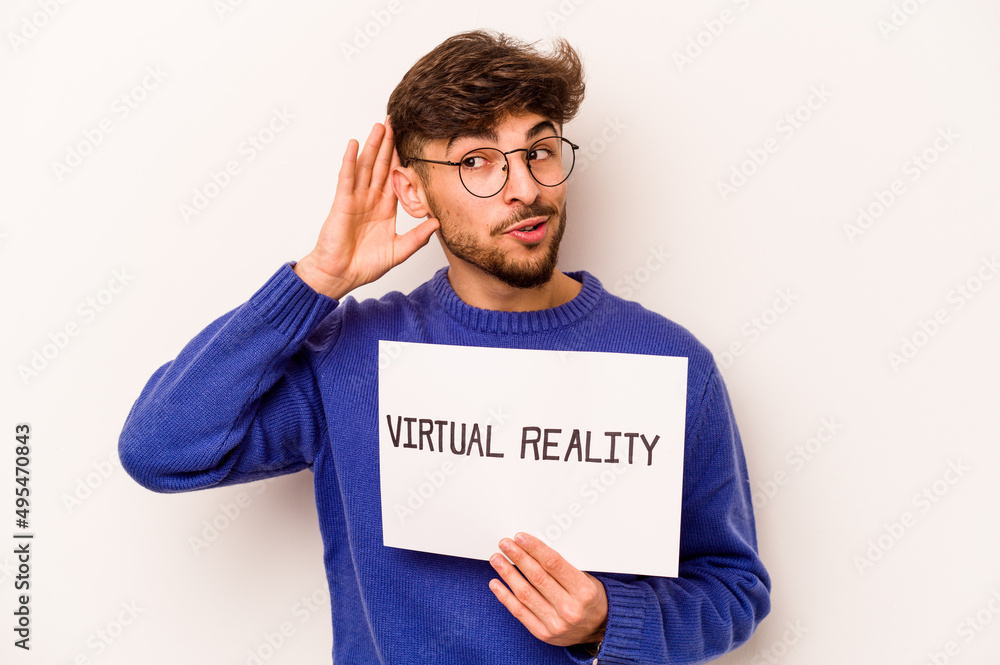 Young hispanic man holding a virtual reality placard isolated on white background trying to listening a gossip. Young hispanic man holding a virtual reality placard isolated on white background trying to listening a gossip.