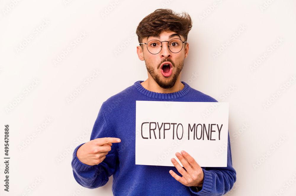 Young hispanic man holding a crypto money placard isolated on white background pointing to the side Young hispanic man holding a crypto money placard isolated on white background pointing to the side