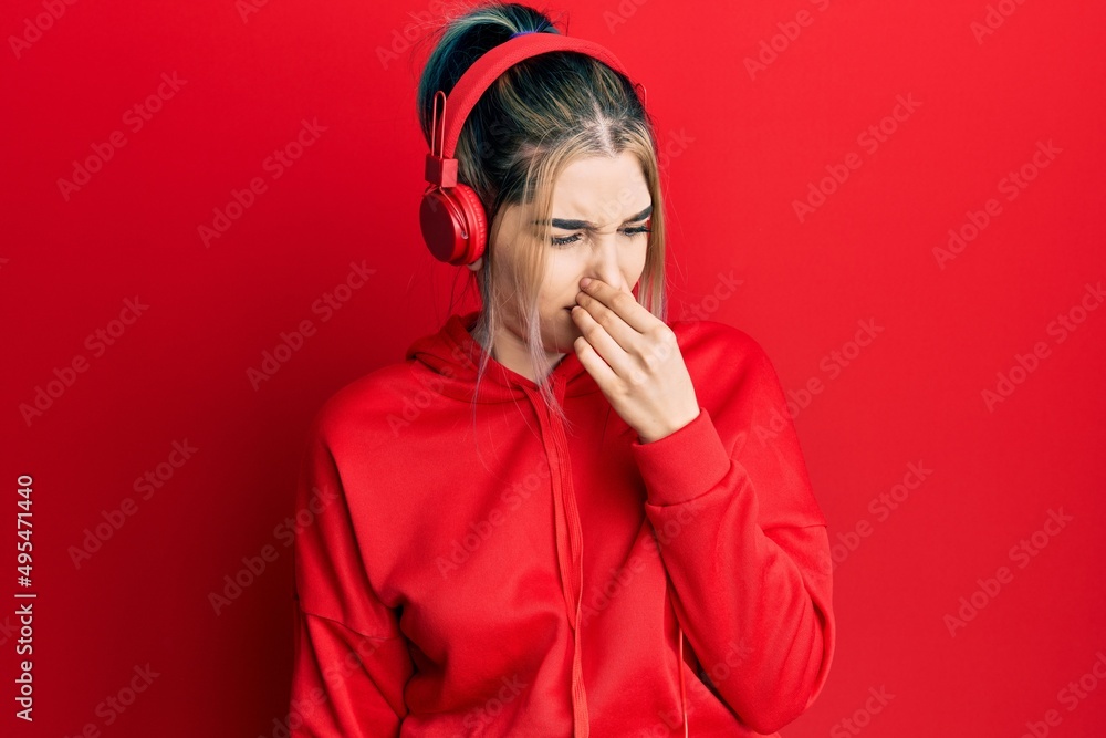 Young modern girl wearing gym clothes and using headphones smelling