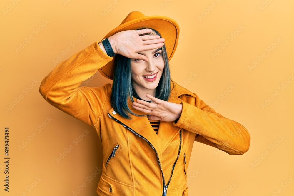 Young modern girl wearing yellow hat and leather jacket smiling cheerful playing peek a boo with hands showing face. surprised and exited Young modern girl wearing yellow hat and leather jacket smiling cheerful playing peek a boo with hands showing face. surprised and exited