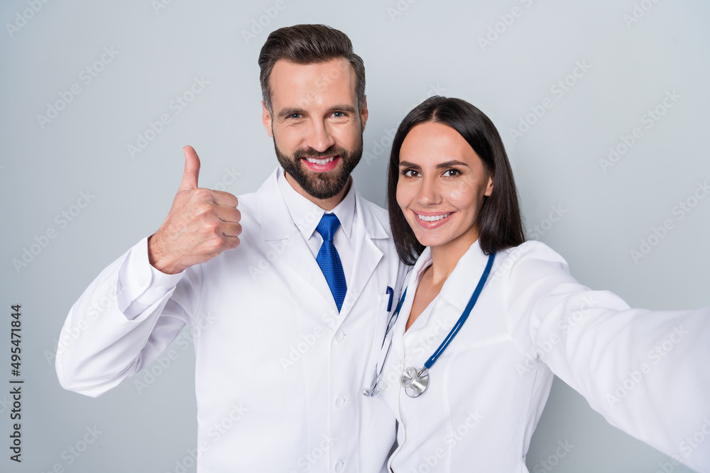 Self-portrait of two attractive cheerful docs therapists bonding showing thumbup team career isolated over grey color pastel background Self-portrait of two attractive cheerful docs therapists bonding showing thumbup team career isolated over grey color pastel background