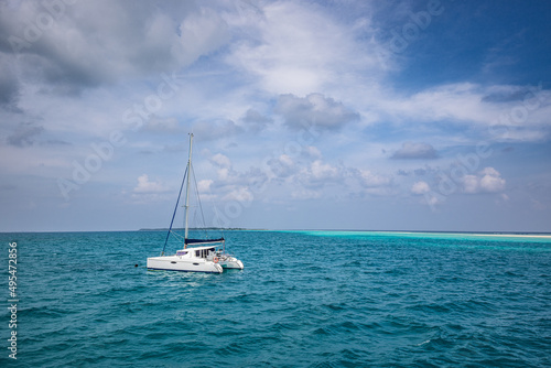 Beautiful turquoise water around white sailboat anchored in middle of ocean. Cloudy sky, ocean lagoon. Adventure travel, recreational seascape. Luxury activity, white yacht