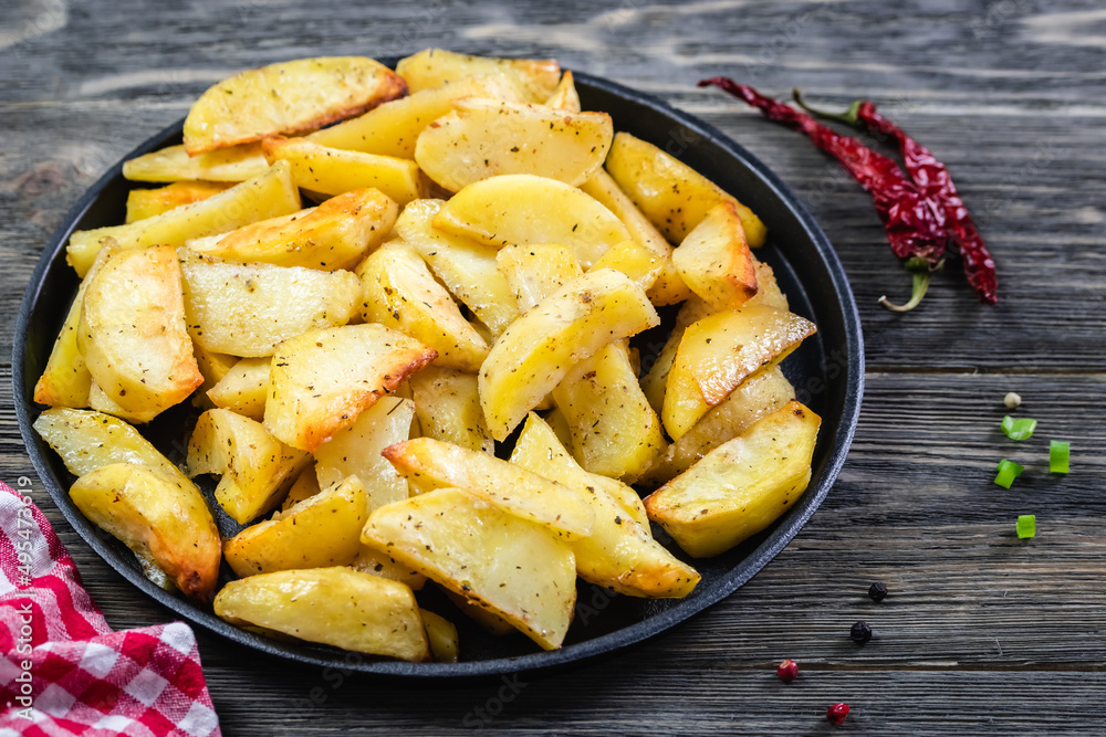 Crispy parmesan rosemary potato wedges in cast iron skillet on wooden background. Top view, copy space, flat lay. Crispy parmesan rosemary potato wedges in cast iron skillet on wooden background. Top view, copy space, flat lay.