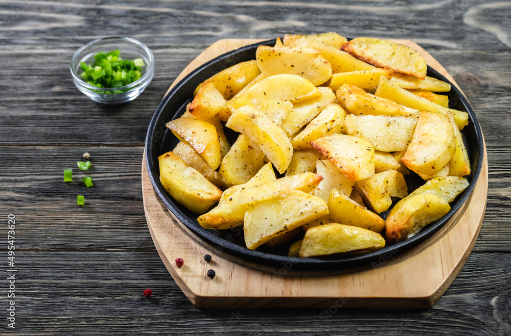 Baked garlic parmesan potato wedges in cast iron skillet on wooden background. Top view, copy space, flat lay. Baked garlic parmesan potato wedges in cast iron skillet on wooden background. Top view, copy space, flat lay.