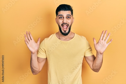 Handsome man with beard wearing casual yellow t shirt celebrating crazy and amazed for success with arms raised and open eyes screaming excited. winner concept © Krakenimages.com
