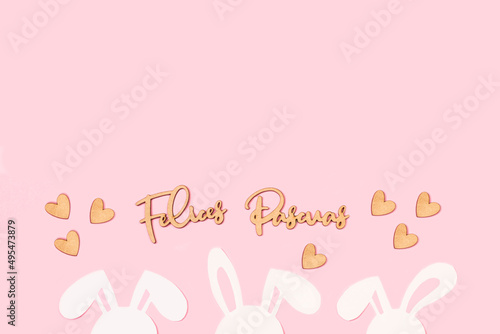 Felices pascuas escrito con letras de madera junto a orejas de conejos y corazones de madera sobre un fondo rosa pastel liso y aislado. Vsta superior y de cerca. Copy space photo