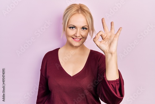Young blonde woman wearing casual winter sweater smiling positive doing ok sign with hand and fingers. successful expression.